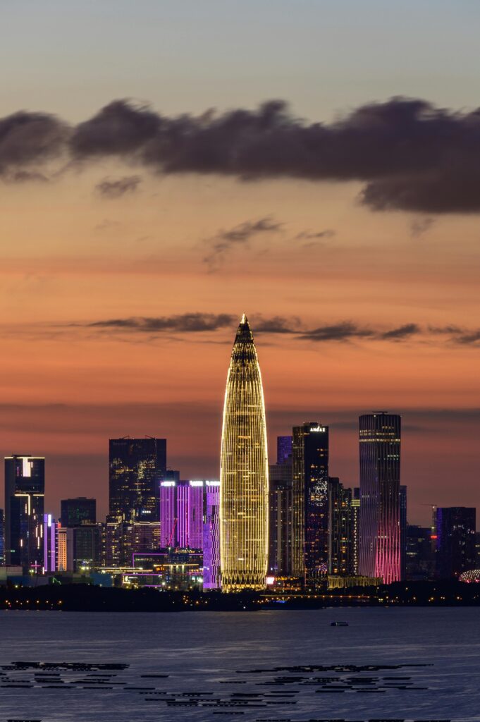 pexels-photo-12668188-12668188 Illuminated city skyline featuring a distinct tall building at sunset.